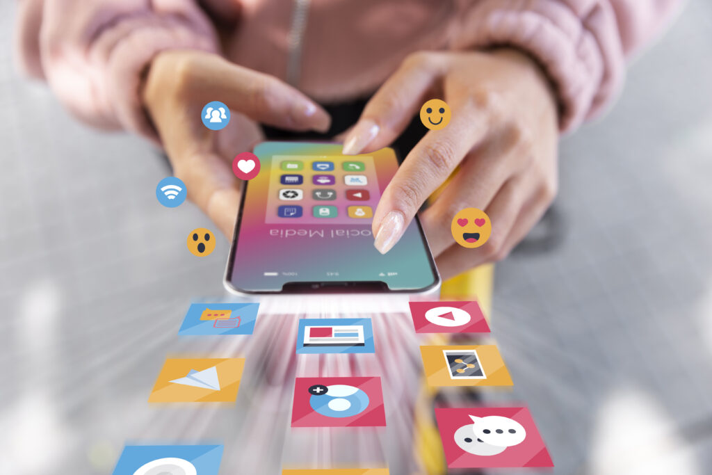 gestao-de-redes-sociais-mao-com-telemovel-e-icones-social-media Mãos a interagir com telemovel com icones de social media a fazer Gestão de Redes Sociais